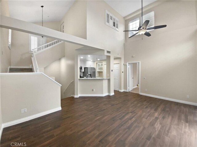 unfurnished living room featuring ceiling fan, dark hardwood / wood-style flooring, and a towering ceiling