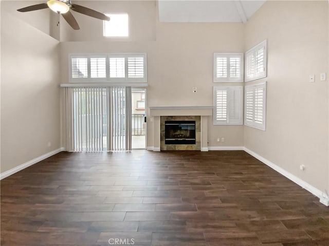 unfurnished living room with a tile fireplace, dark hardwood / wood-style flooring, ceiling fan, and high vaulted ceiling