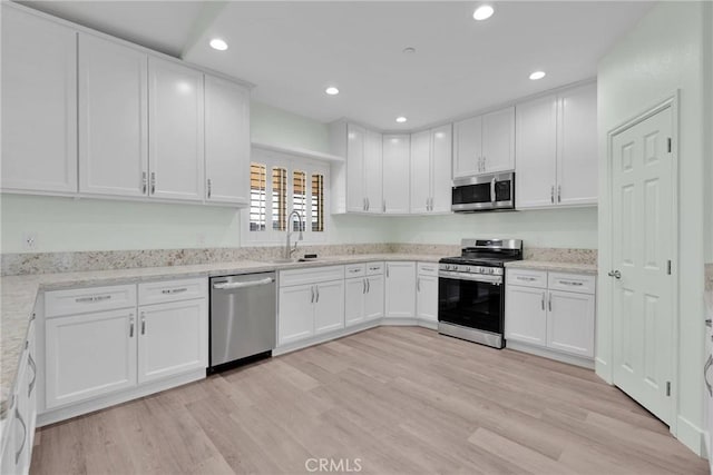 kitchen with white cabinetry, sink, stainless steel appliances, light stone countertops, and light wood-type flooring