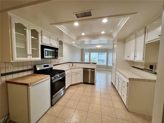 kitchen featuring light tile patterned flooring, white cabinetry, appliances with stainless steel finishes, a raised ceiling, and backsplash