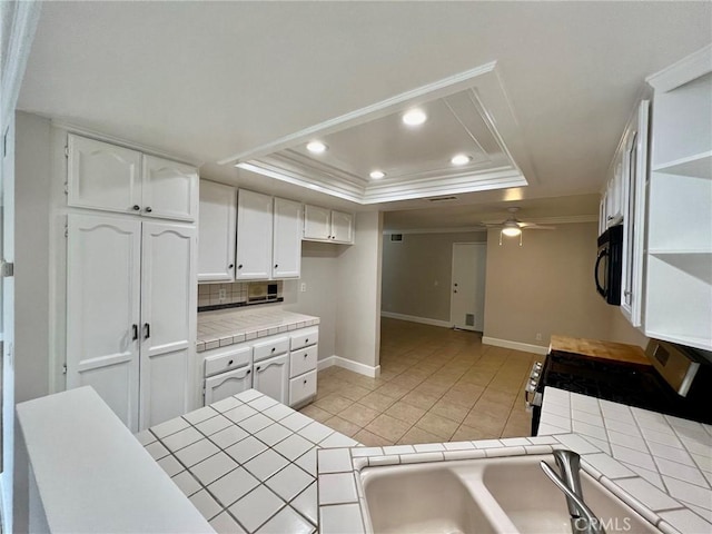 kitchen featuring white cabinetry, a tray ceiling, tile counters, and stainless steel range with gas stovetop