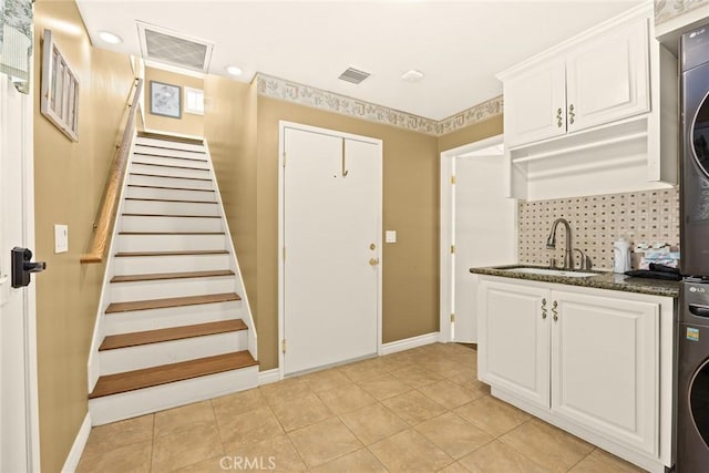 kitchen with white cabinetry, sink, dark stone countertops, backsplash, and stacked washer and clothes dryer