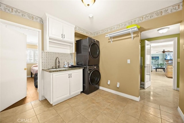 clothes washing area featuring stacked washer and dryer, sink, light tile patterned floors, and cabinets