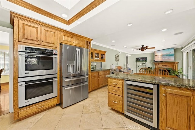 kitchen with ornamental molding, appliances with stainless steel finishes, beverage cooler, and dark stone counters