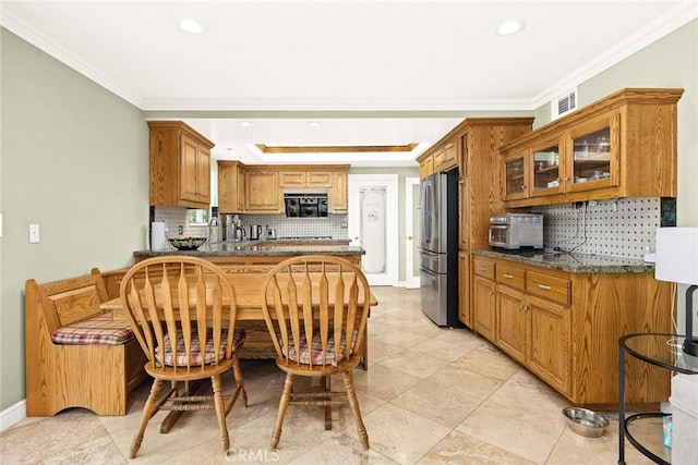 kitchen featuring tasteful backsplash, stainless steel refrigerator, ornamental molding, a tray ceiling, and dark stone counters