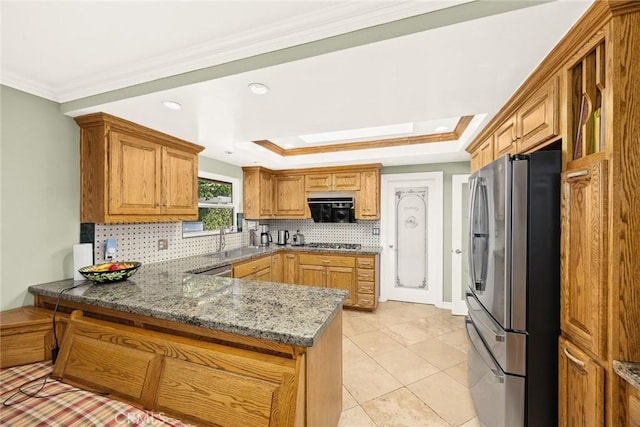 kitchen featuring dark stone countertops, a tray ceiling, kitchen peninsula, and appliances with stainless steel finishes