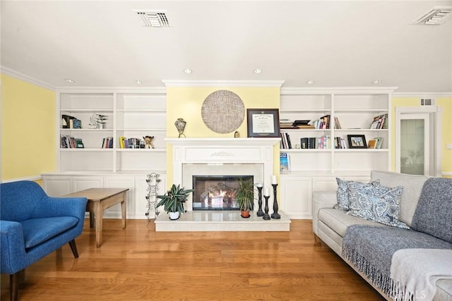 living room with built in shelves, ornamental molding, and light hardwood / wood-style floors