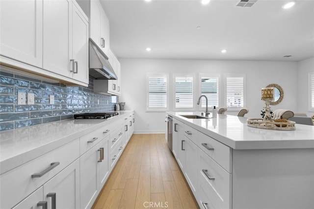 kitchen with white cabinetry, sink, decorative backsplash, stainless steel appliances, and a center island with sink