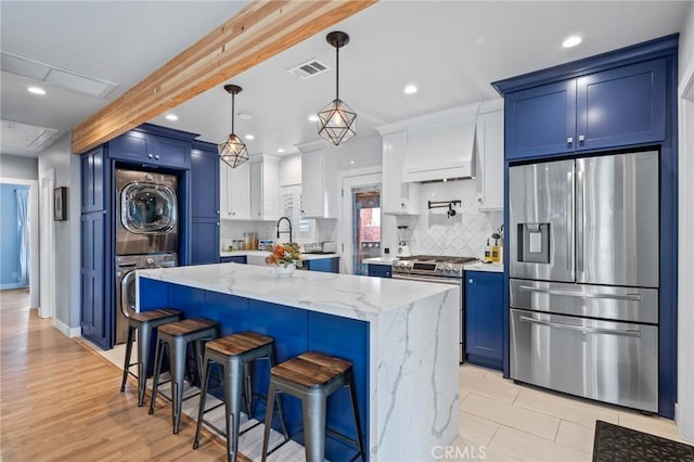 kitchen featuring stainless steel appliances, stacked washer / dryer, and blue cabinets