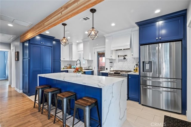 kitchen featuring blue cabinetry, decorative light fixtures, appliances with stainless steel finishes, custom range hood, and white cabinets