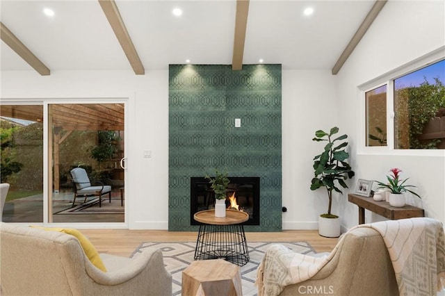 living room featuring beam ceiling, wood-type flooring, and a large fireplace