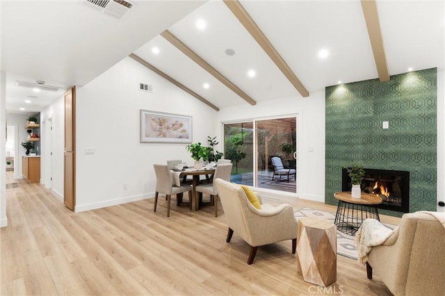 living room with a large fireplace, vaulted ceiling with beams, and light wood-type flooring