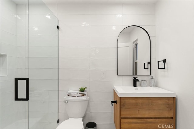 bathroom with vanity, toilet, a shower with shower door, and tile walls