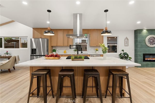 kitchen with stainless steel refrigerator with ice dispenser, a spacious island, stovetop, island range hood, and pendant lighting