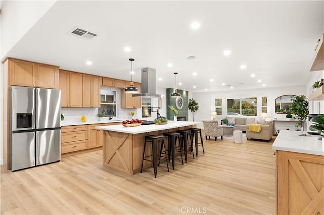 kitchen with stainless steel refrigerator with ice dispenser, island range hood, decorative light fixtures, a kitchen breakfast bar, and a kitchen island