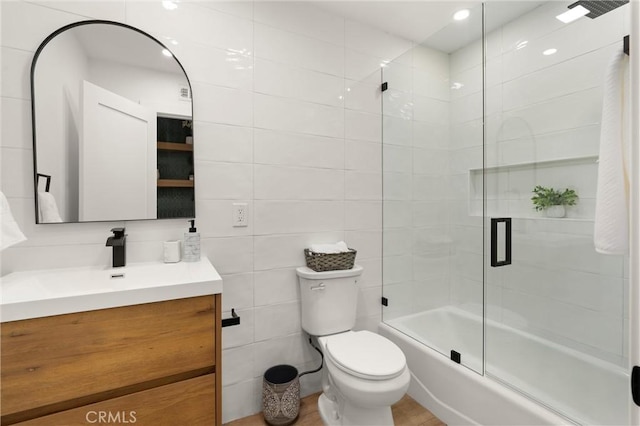 full bathroom with enclosed tub / shower combo, tile walls, vanity, and toilet