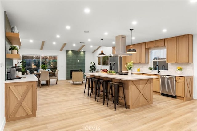 kitchen with island range hood, hanging light fixtures, a center island, stainless steel dishwasher, and light hardwood / wood-style floors