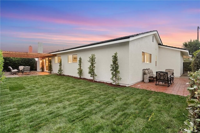 back house at dusk featuring a yard, a pergola, and a patio