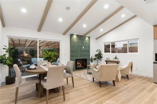 dining space with a tiled fireplace, vaulted ceiling with beams, and light wood-type flooring