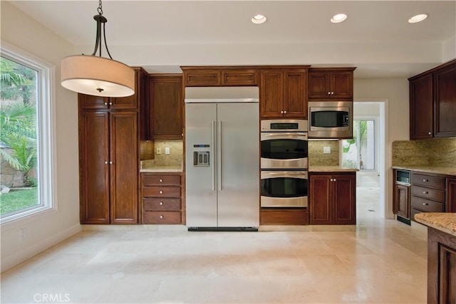 kitchen with light stone counters, a healthy amount of sunlight, built in appliances, and decorative light fixtures