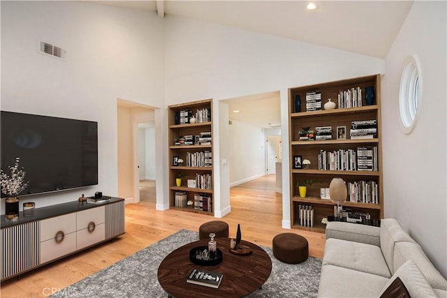 living room with high vaulted ceiling, light wood-type flooring, and built in shelves