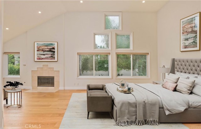 bedroom featuring lofted ceiling, a tiled fireplace, and light hardwood / wood-style floors