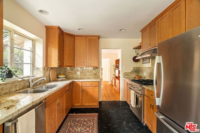 kitchen with stainless steel appliances, light stone countertops, sink, and backsplash