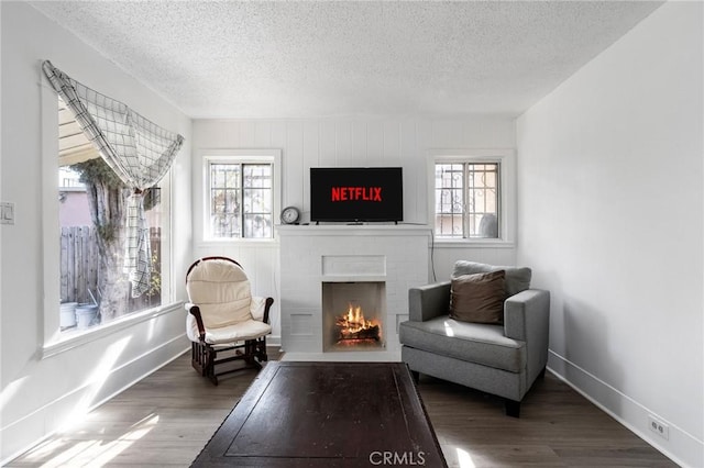 living area featuring wood-type flooring, a brick fireplace, and a textured ceiling