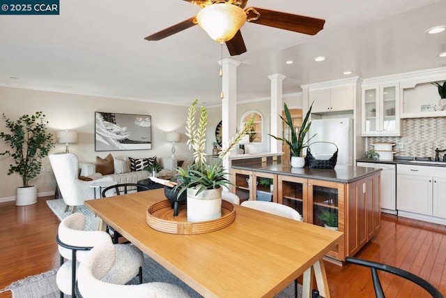 dining room featuring decorative columns, sink, hardwood / wood-style floors, and ceiling fan