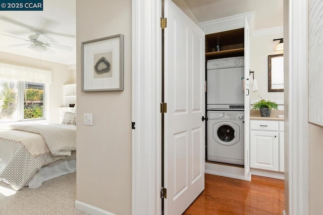 laundry area featuring stacked washer and dryer, ornamental molding, hardwood / wood-style flooring, and ceiling fan