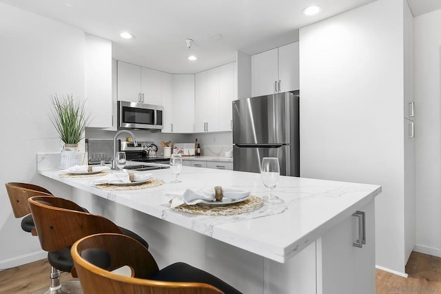 kitchen with stainless steel appliances, white cabinetry, a breakfast bar, and kitchen peninsula