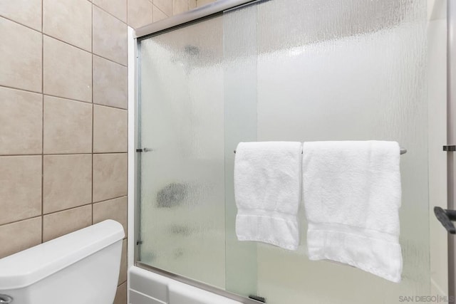 bathroom featuring shower / bath combination with glass door, toilet, and tile walls