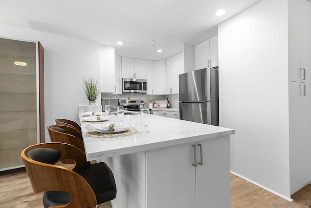 kitchen featuring sink, light hardwood / wood-style flooring, appliances with stainless steel finishes, light stone counters, and white cabinets