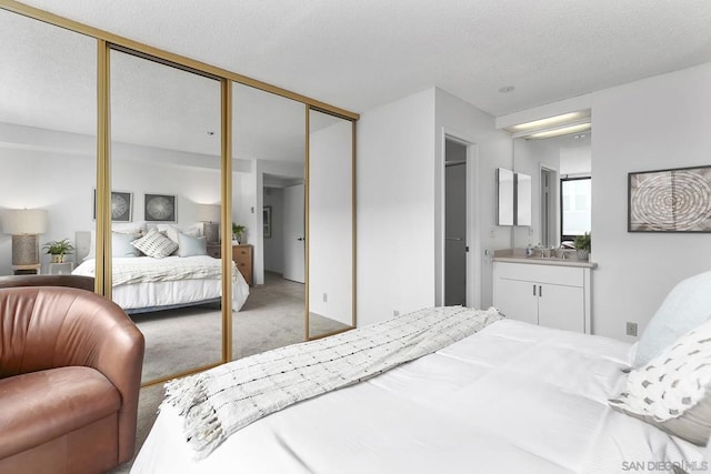 bedroom with connected bathroom, sink, light carpet, a textured ceiling, and a closet