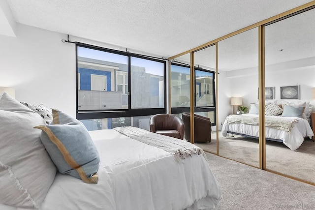 carpeted bedroom with a textured ceiling, a wall of windows, and a closet