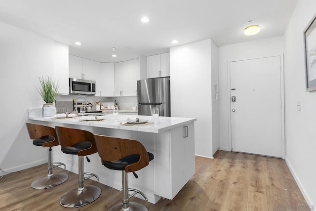 kitchen featuring sink, a breakfast bar, appliances with stainless steel finishes, white cabinets, and kitchen peninsula