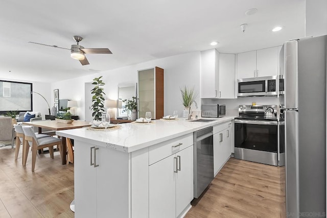 kitchen with sink, white cabinetry, light wood-type flooring, kitchen peninsula, and stainless steel appliances