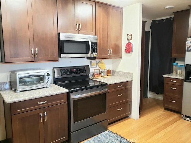 kitchen featuring dark brown cabinetry, light stone counters, light hardwood / wood-style flooring, and appliances with stainless steel finishes