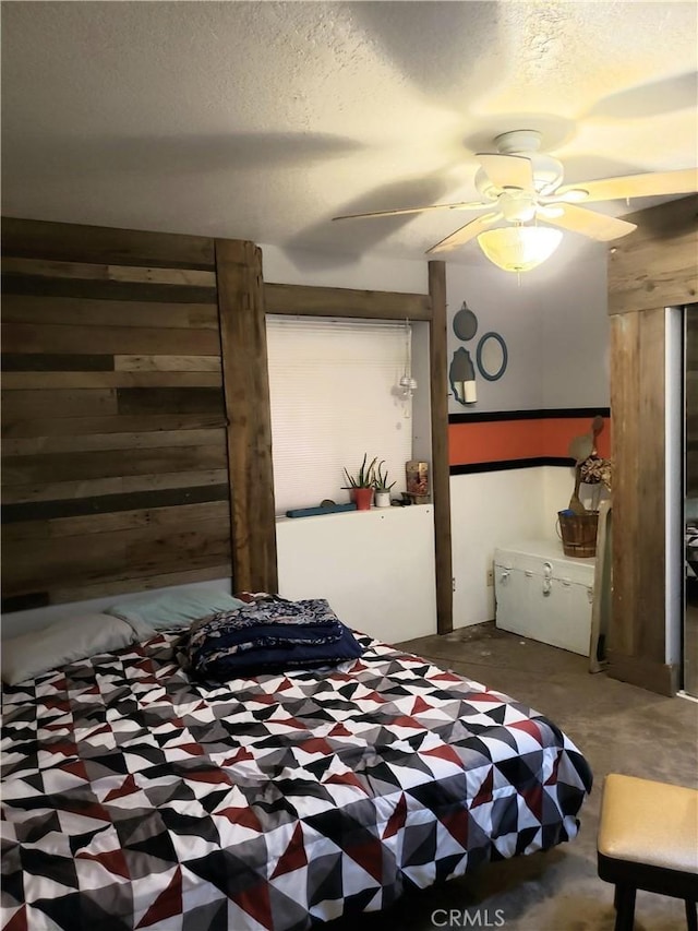 bedroom with ceiling fan, wooden walls, concrete flooring, and a textured ceiling