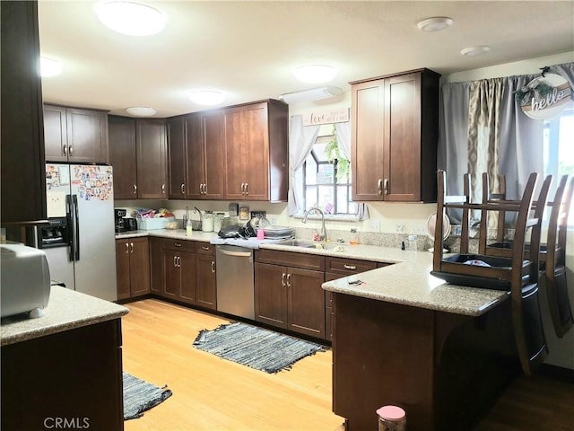 kitchen featuring sink, appliances with stainless steel finishes, dark brown cabinets, light hardwood / wood-style floors, and kitchen peninsula