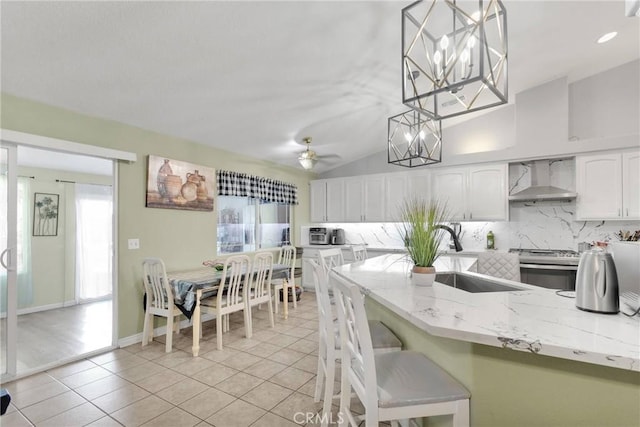 kitchen with white cabinetry, decorative backsplash, stainless steel range oven, decorative light fixtures, and wall chimney exhaust hood