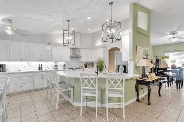 kitchen featuring stainless steel fridge, a breakfast bar, white cabinetry, hanging light fixtures, and wall chimney exhaust hood