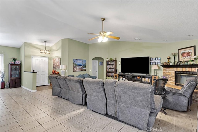 tiled living room with a fireplace, ceiling fan, and vaulted ceiling