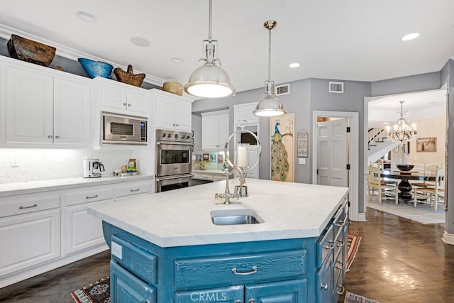 kitchen with appliances with stainless steel finishes, blue cabinets, an island with sink, and white cabinets