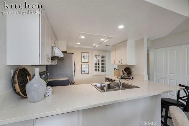 kitchen with a breakfast bar, sink, white cabinets, stove, and kitchen peninsula