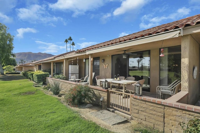 rear view of house with a mountain view, a patio area, ceiling fan, and a lawn