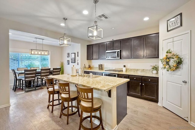 kitchen with dark brown cabinetry, sink, decorative light fixtures, an island with sink, and stainless steel appliances