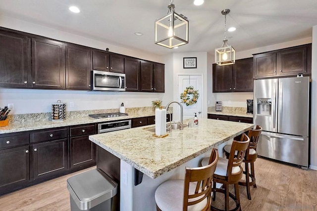 kitchen with appliances with stainless steel finishes, pendant lighting, a center island with sink, and dark brown cabinetry