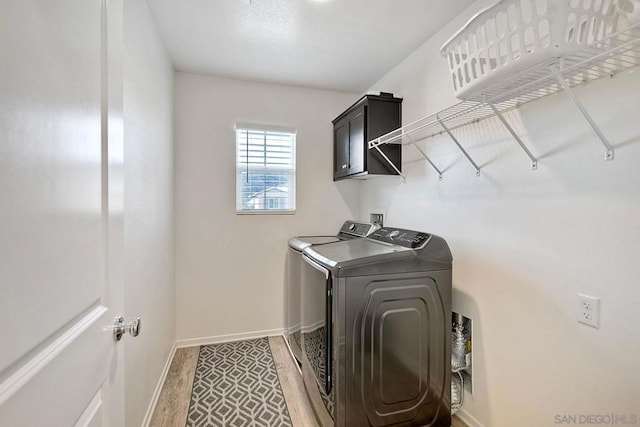 clothes washing area featuring washer and clothes dryer, cabinets, and wood-type flooring