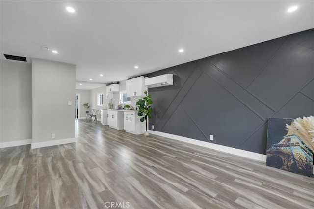 unfurnished living room with light wood-type flooring and an AC wall unit